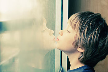 Niño pequeño con necesidades especiales mirando por la ventana