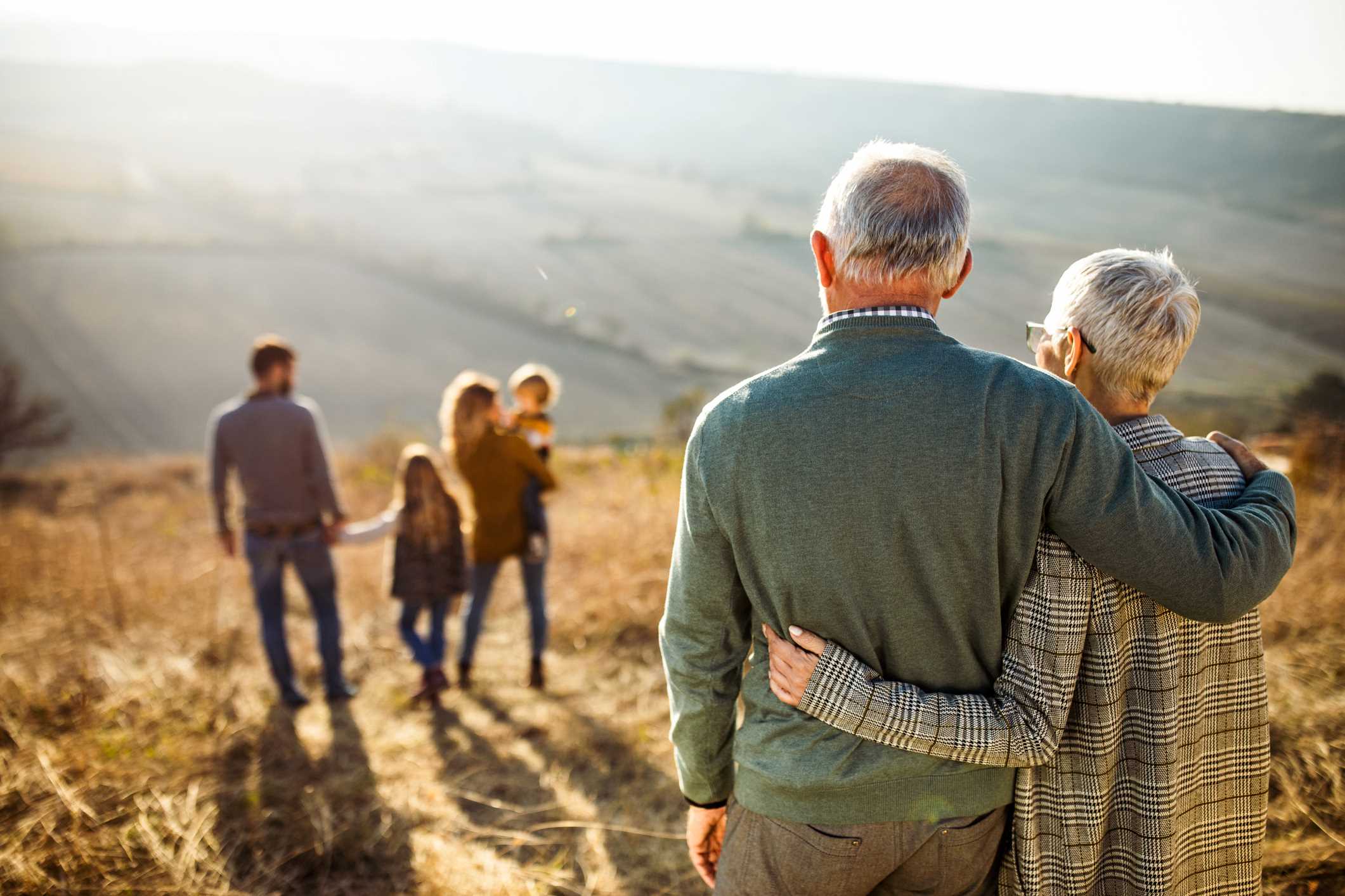 Grandparents embracing as their child's family walks down a hill