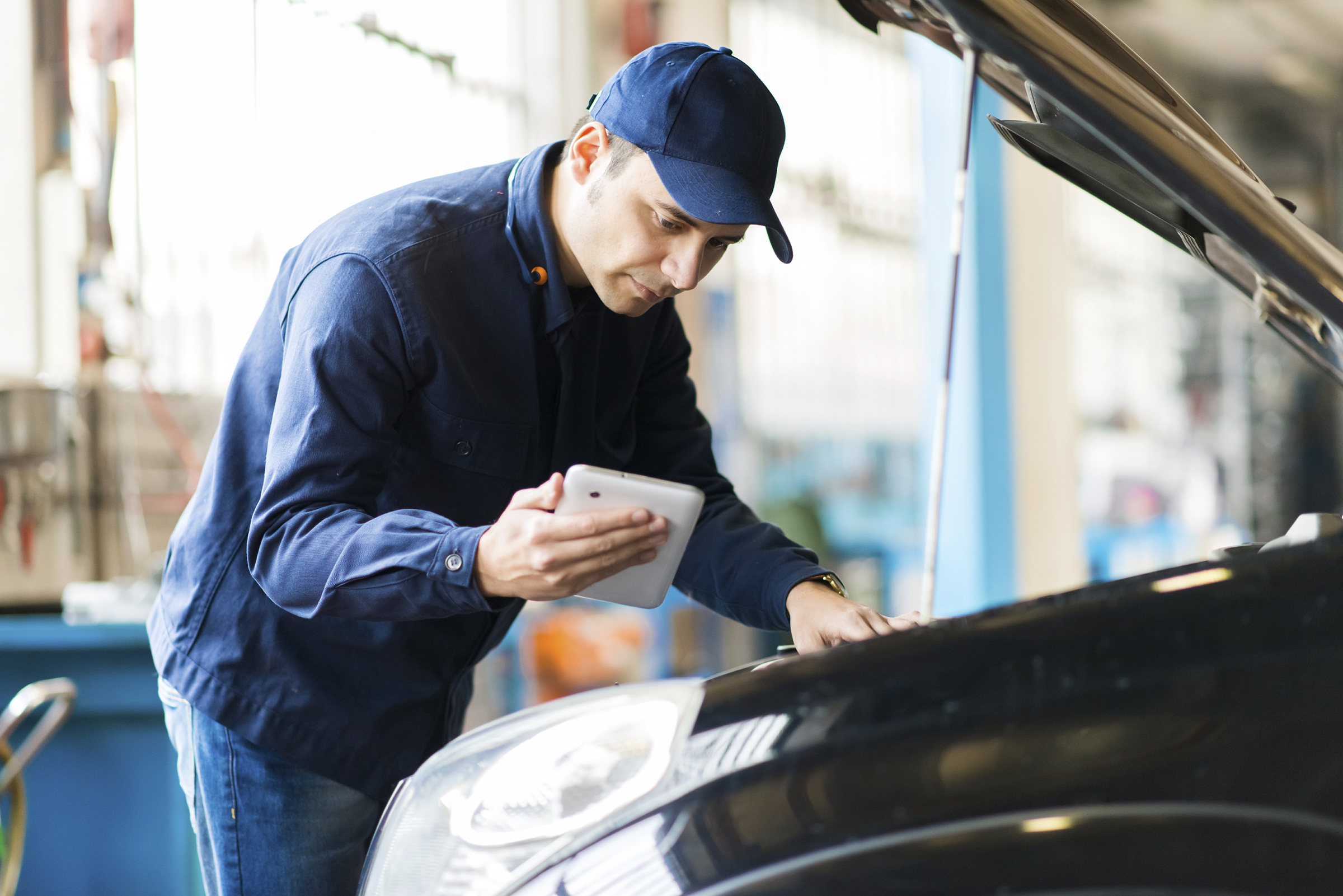 Auto mechanic working on vehicle & looking at data on handheld device