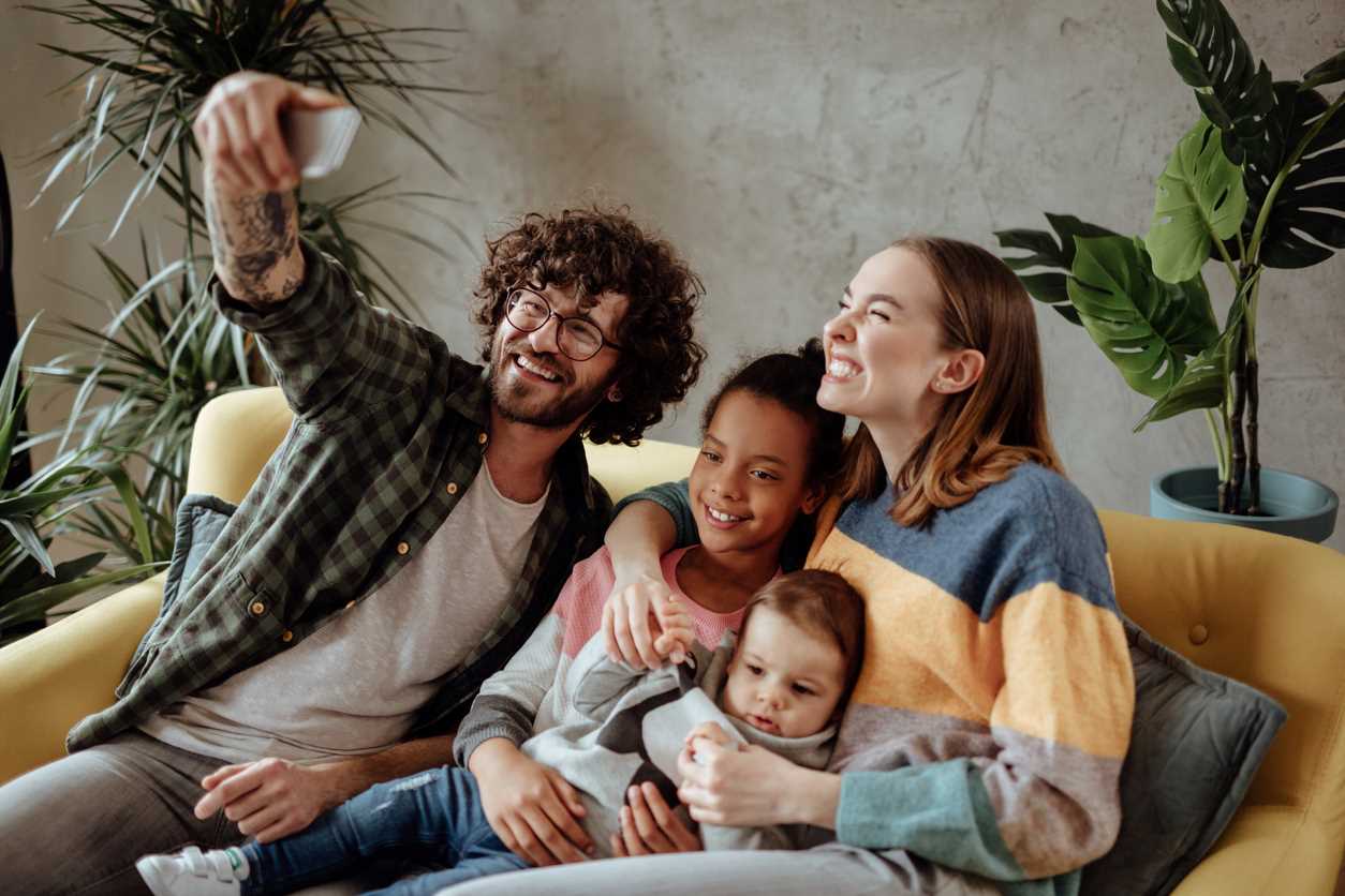 Familia con un niño adoptado tomando una foto mientras se sienta en el sofá