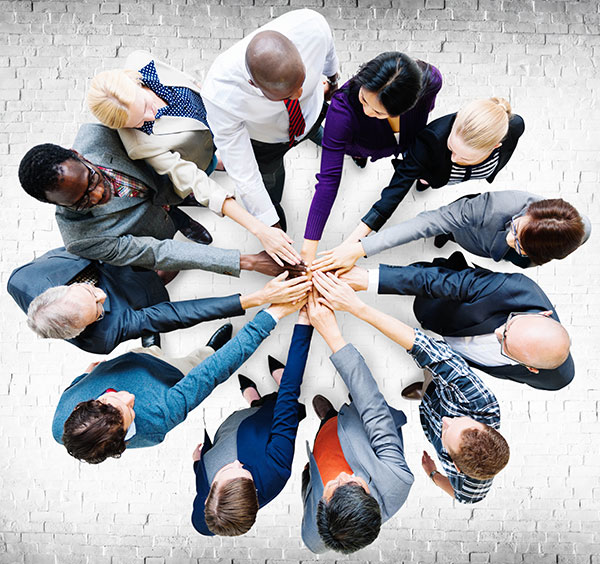 12 business people standing in a circle and stacking their hands