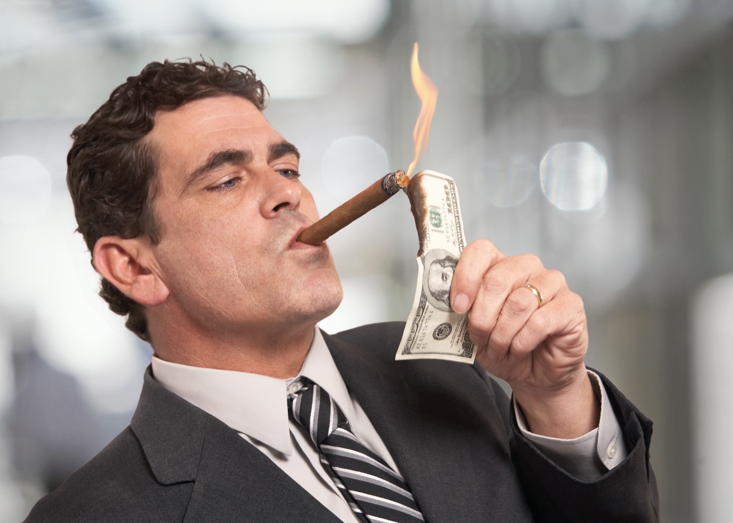 Male lawyer smoking a cigar and burning a hundred dollar bill