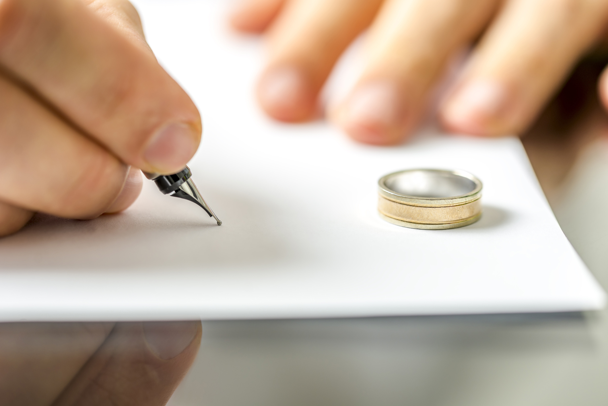 Hombre firmando un documento de divorcio junto al anillo de bodas