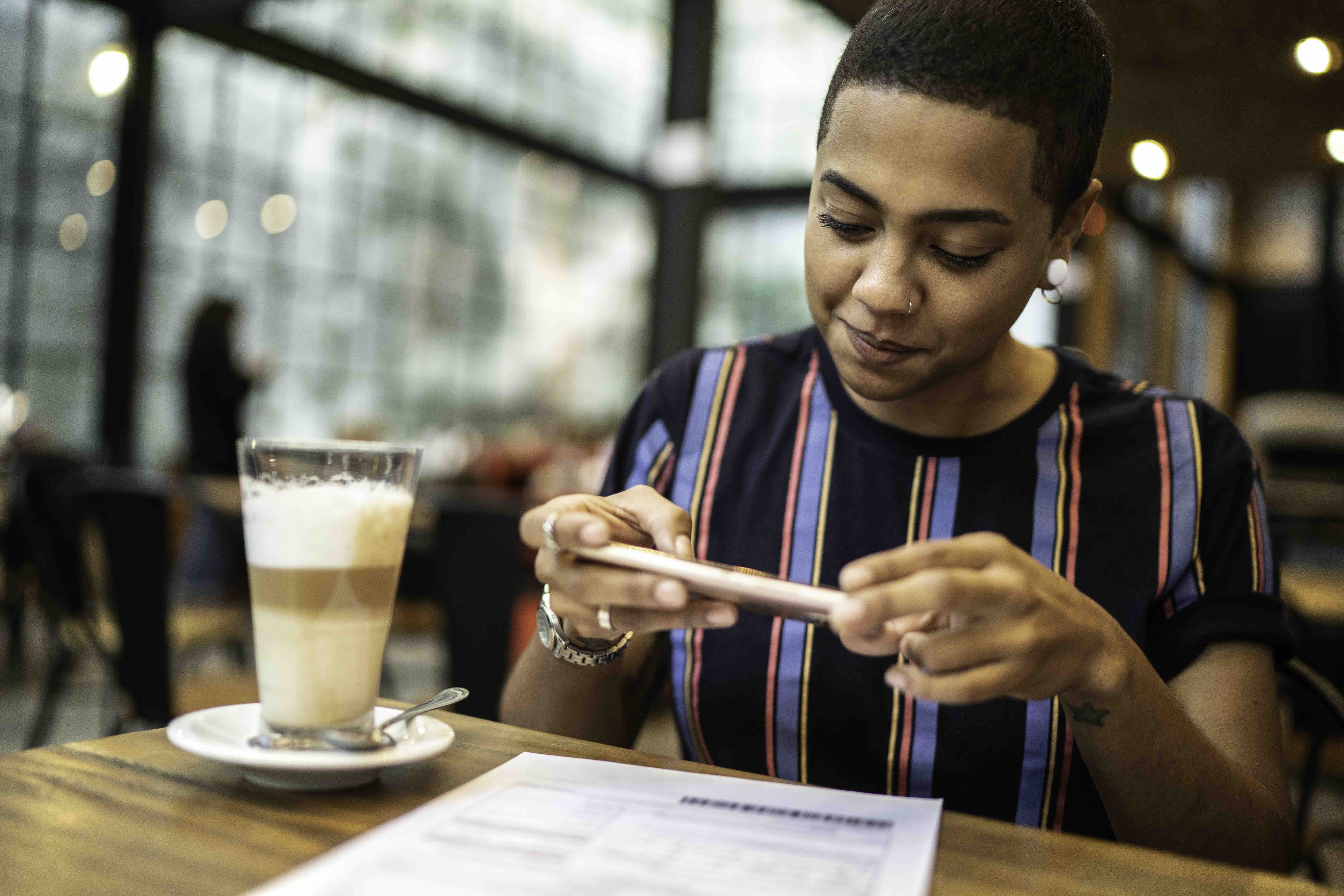 Mujer joven pagando facturas por teléfono en el café