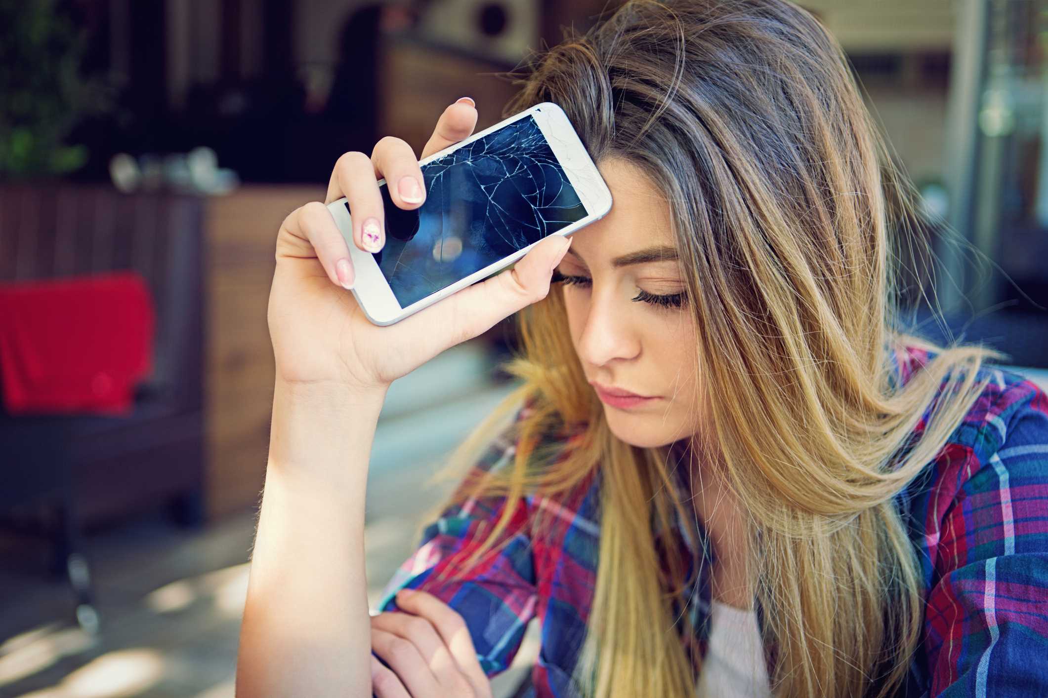 Adolescente sosteniendo un teléfono inteligente destrozado
