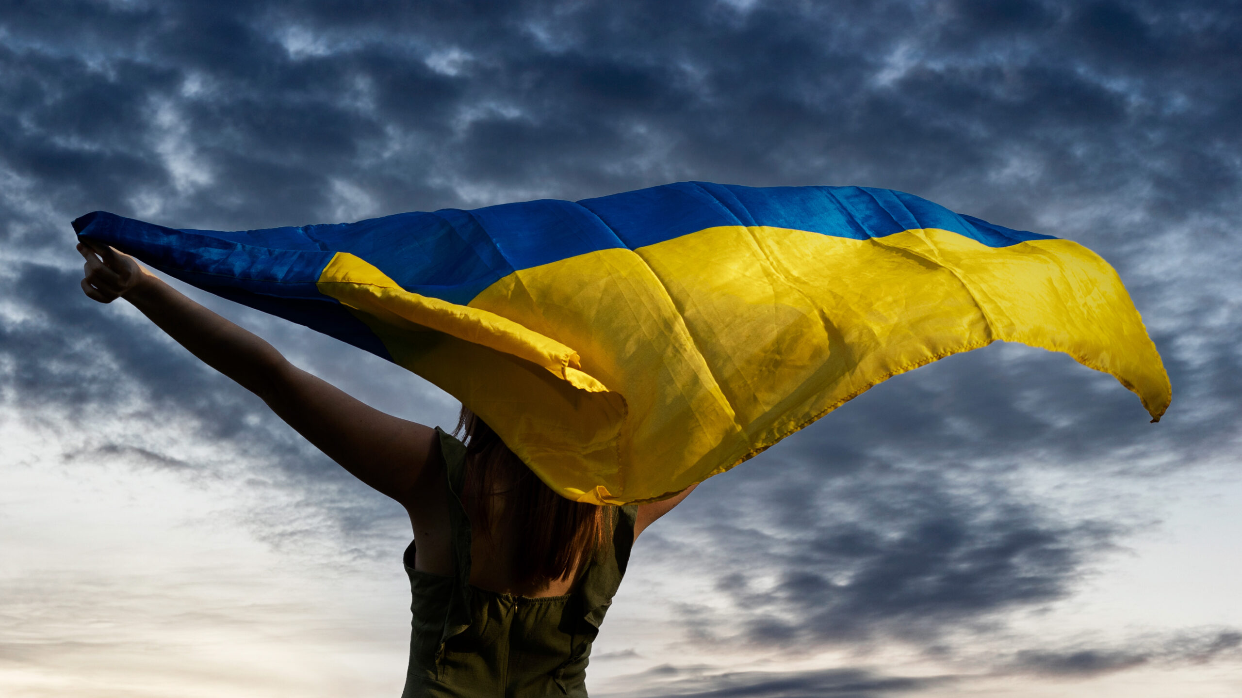 Ukrainian woman proudly holding country's blue and yellow flag outside with clouds in the background