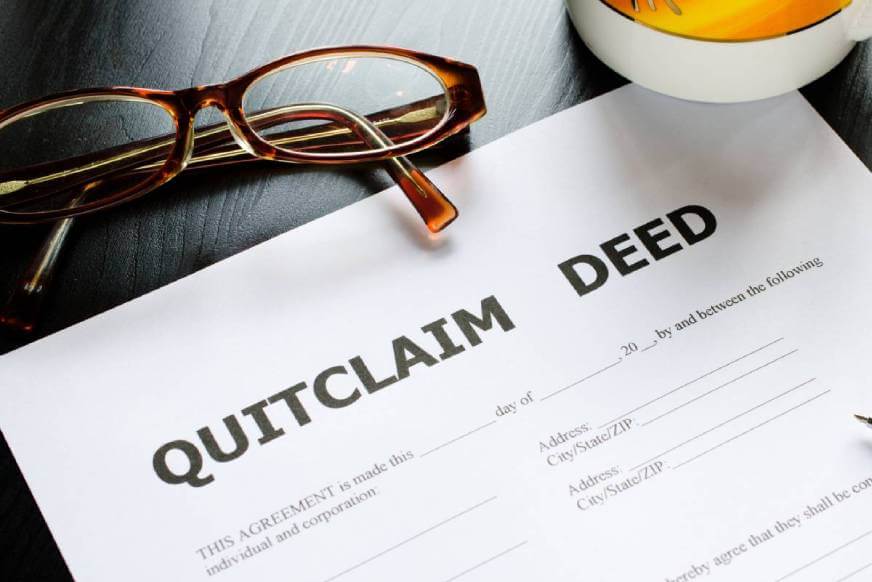 Quitclaim Deed on a desk with eyeglasses and mug nearby.