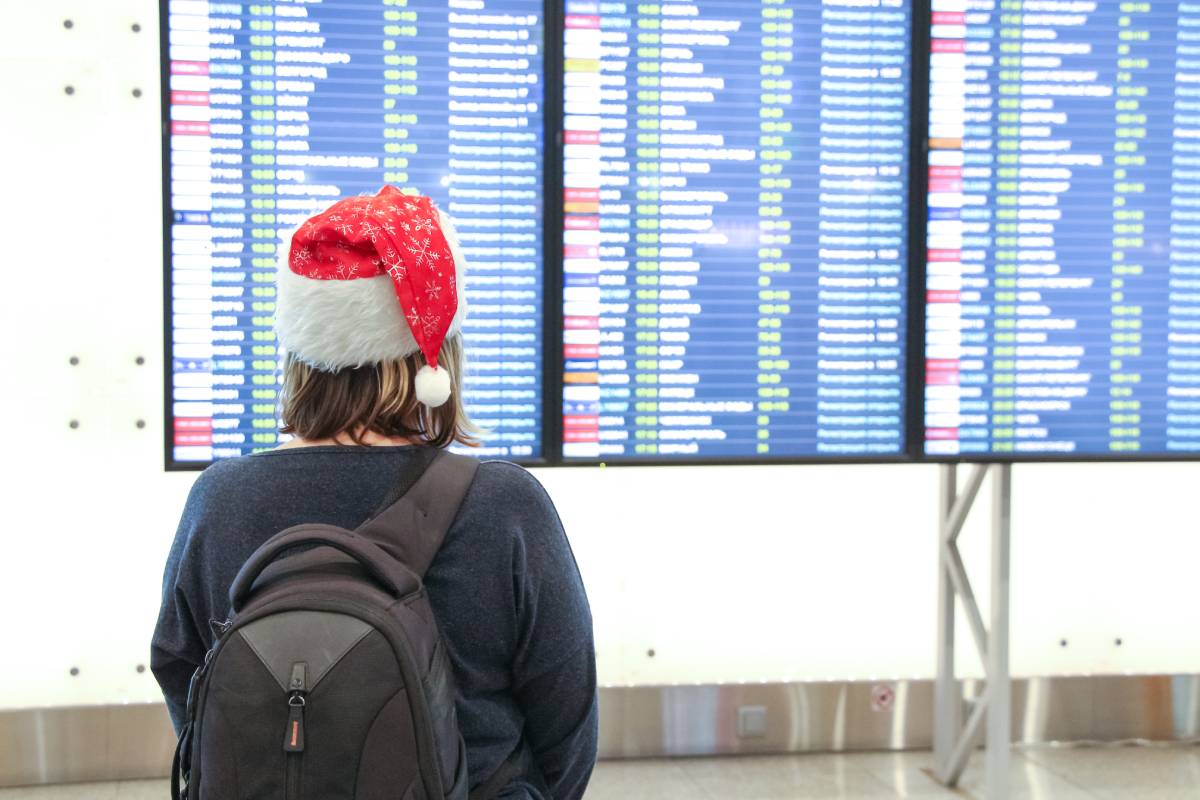 Woman holiday traveler wearing Santa Claus hat looking at airport flight status board.