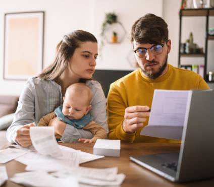 Mother holding baby and she discusses tax extension with father as they sit in front of a laptop computer.
