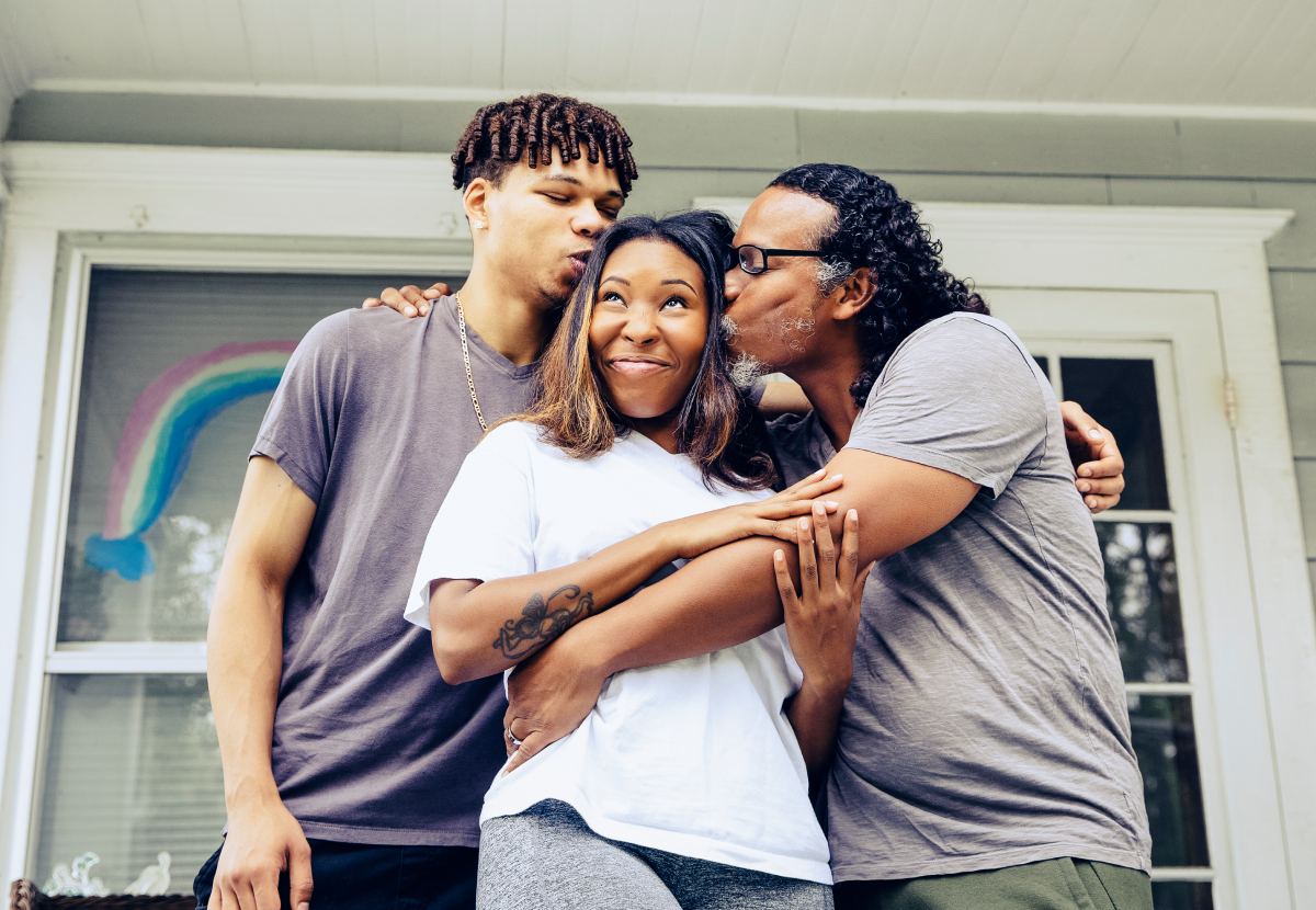 Father kissing his teen daughter as his teenage son stands nearby.