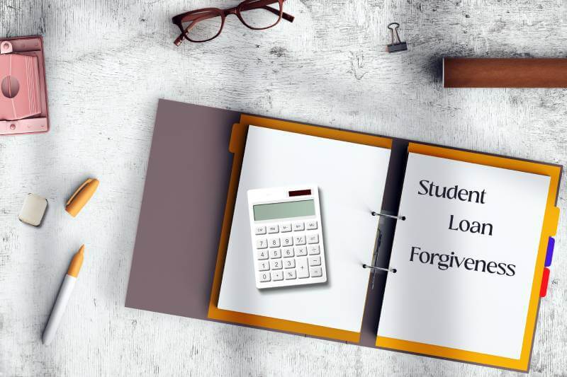 Student Loan Forgiveness notebook, calculator, pen, and eyeglassses on a table.