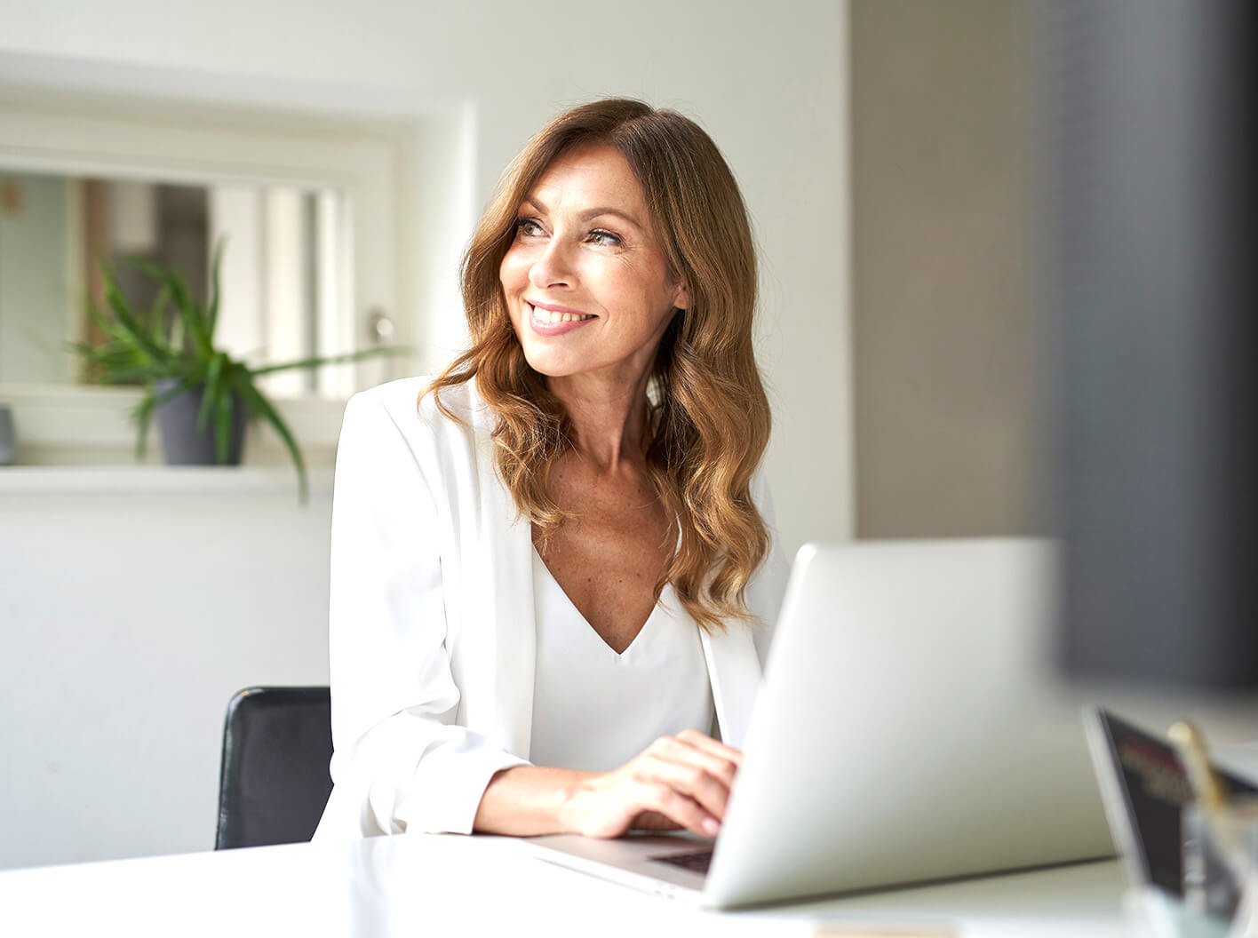 Mujer sonriente trabajando en una computadora portátil en un escritorio de oficina.