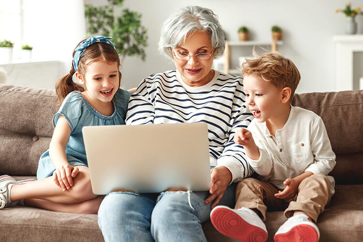 Una mujer sentada en un sofá usa una computadora portátil para buscar un abogado de derecho familiar mientras los niños observan sus acciones con asombro.